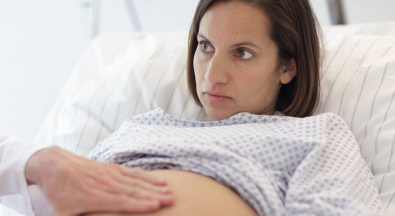 Grávida escuta atentamente explicação médica com mão do profissional de saúde na barriga