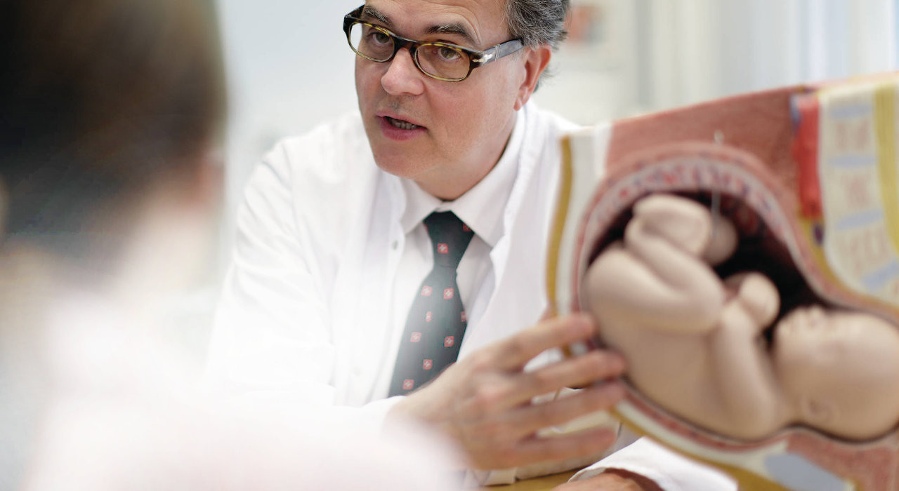 Médico fala com mulher grávida apontando para figura de bebé no útero